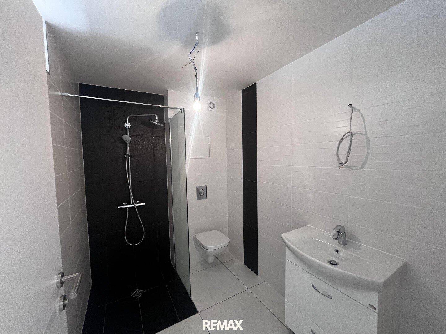 Modernes Badezimmer mit Dusche, WC und Waschbecken, ausgestattet mit weißen und schwarzen Fliesen.
