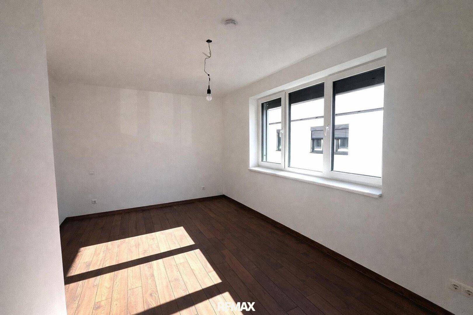 Helles Schlafzimmer mit dunklem Parkettboden und einem großen Fenster für viel Tageslicht.
