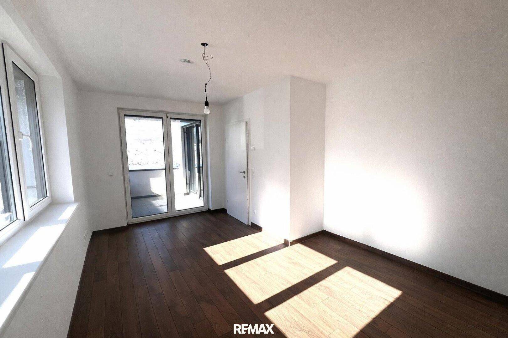 Heller, leerer Raum mit dunklem Parkettboden und direktem Zugang zu einem Balkon.