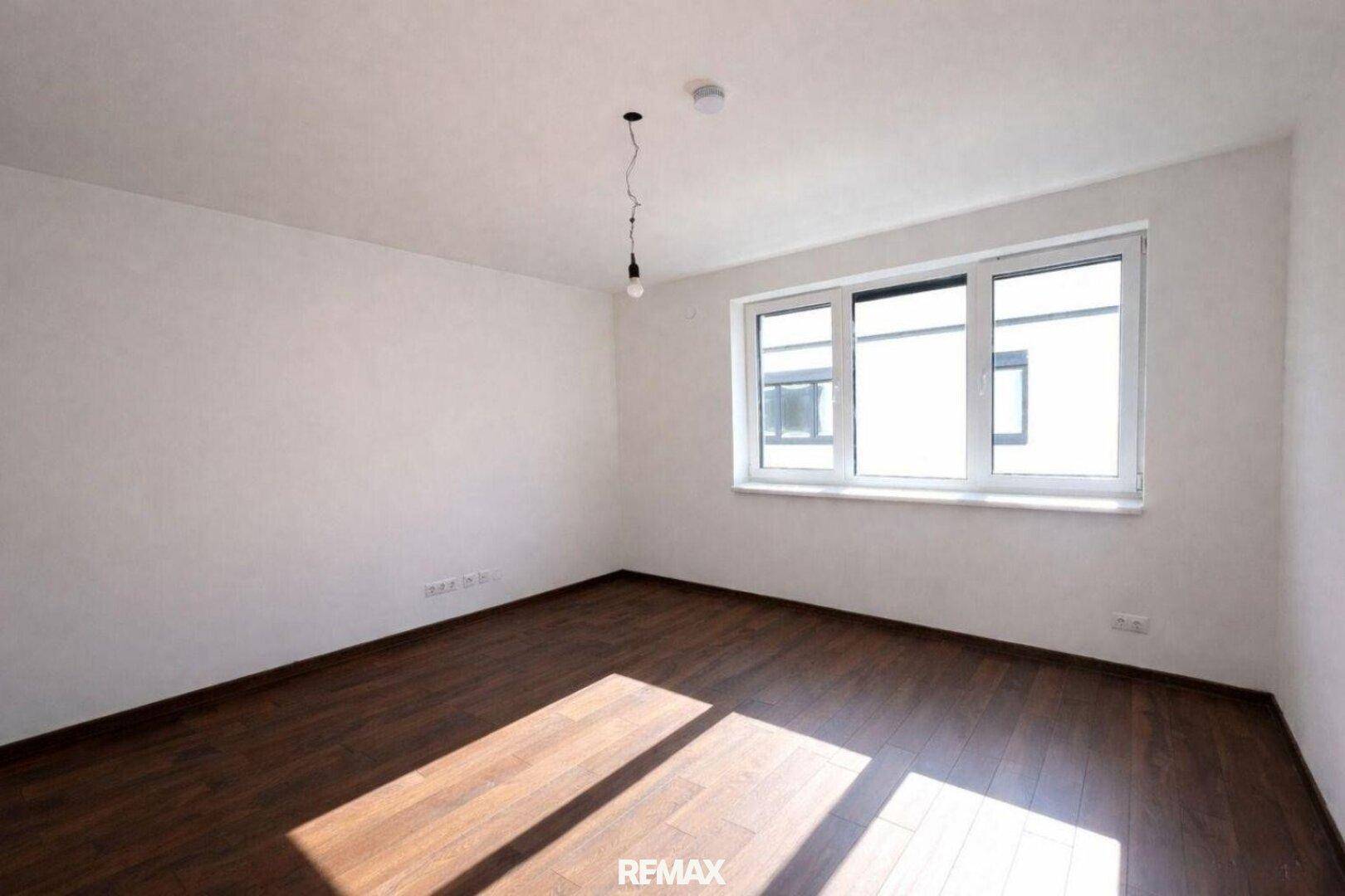 Lichtdurchflutetes Schlafzimmer mit Parkettboden und einem breiten Fenster, ideal für Ruhe.