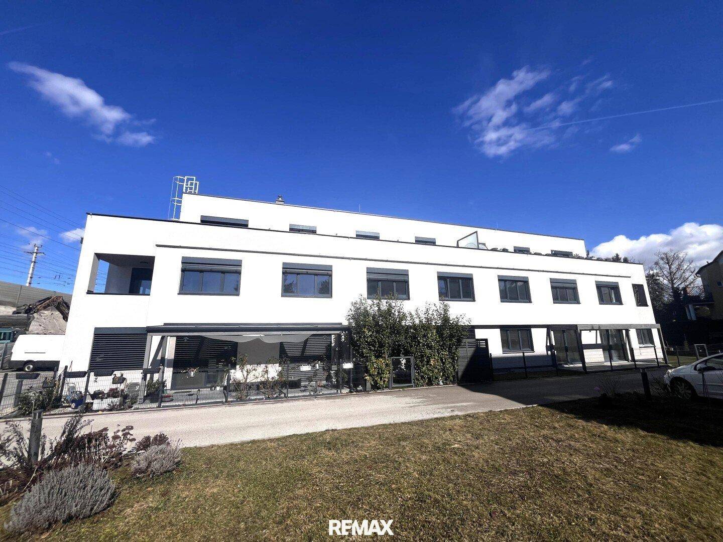 Moderne weiße Fassade eines Neubaus mit großen Fenstern und gepflegter Außenanlage.