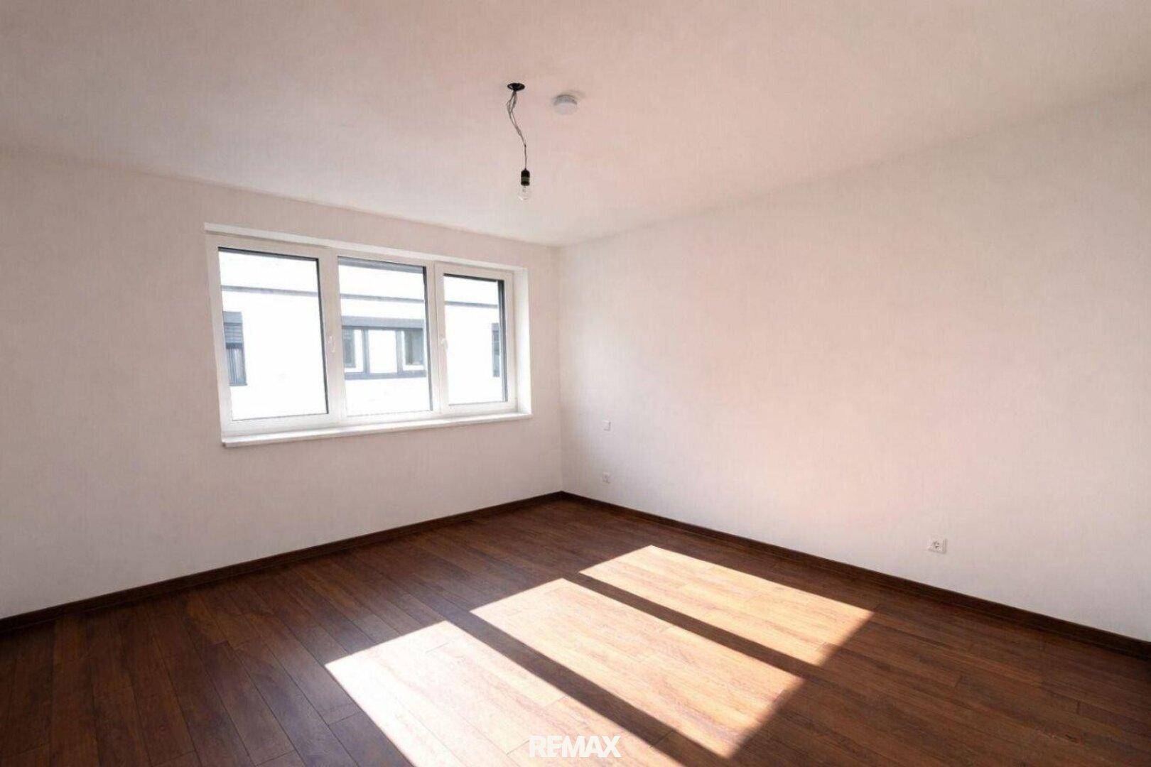 Geräumiges Schlafzimmer mit dunklem Parkettboden und einem großen Fenster, das viel Licht hereinlässt.