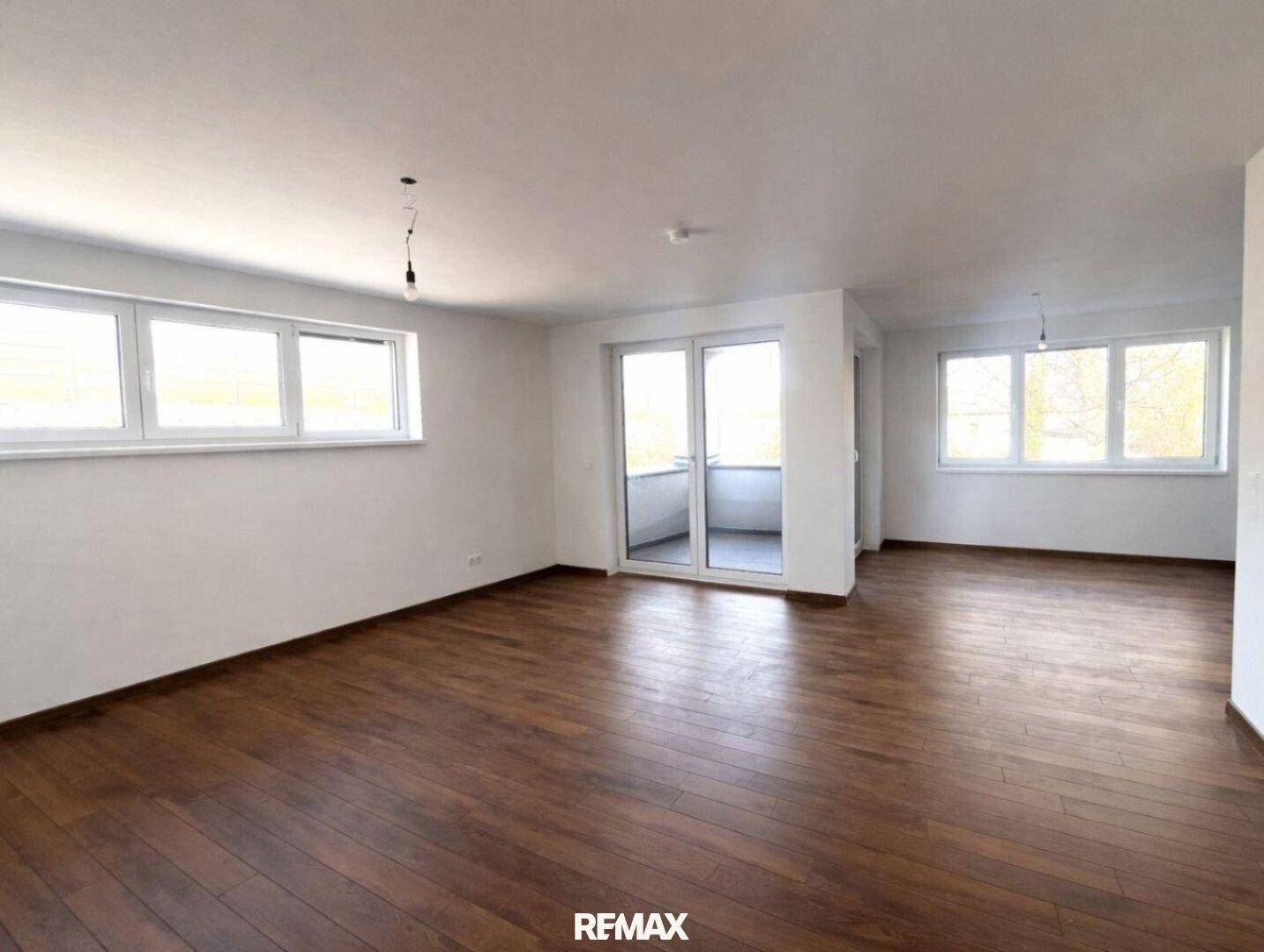 Großzügiges Wohnzimmer mit Holzboden und vielen Fenstern für viel Tageslicht.