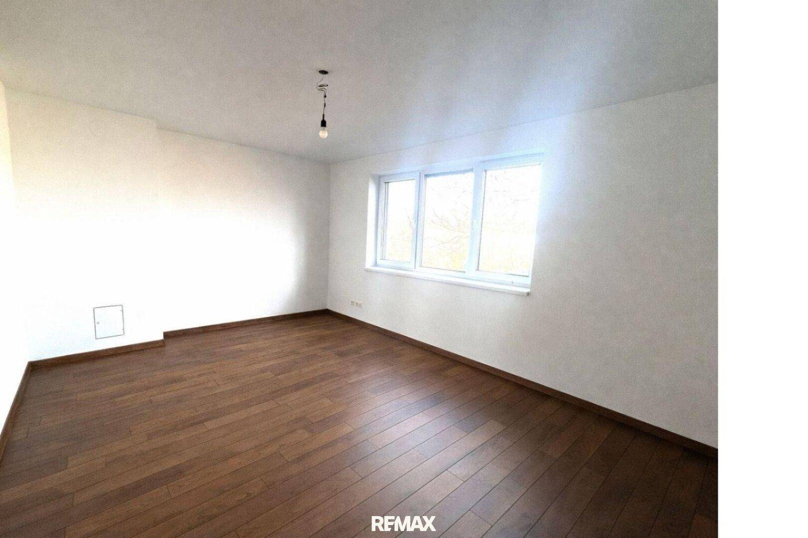 Helles Schlafzimmer mit Holzboden und großem Fenster, bereit zur individuellen Gestaltung.