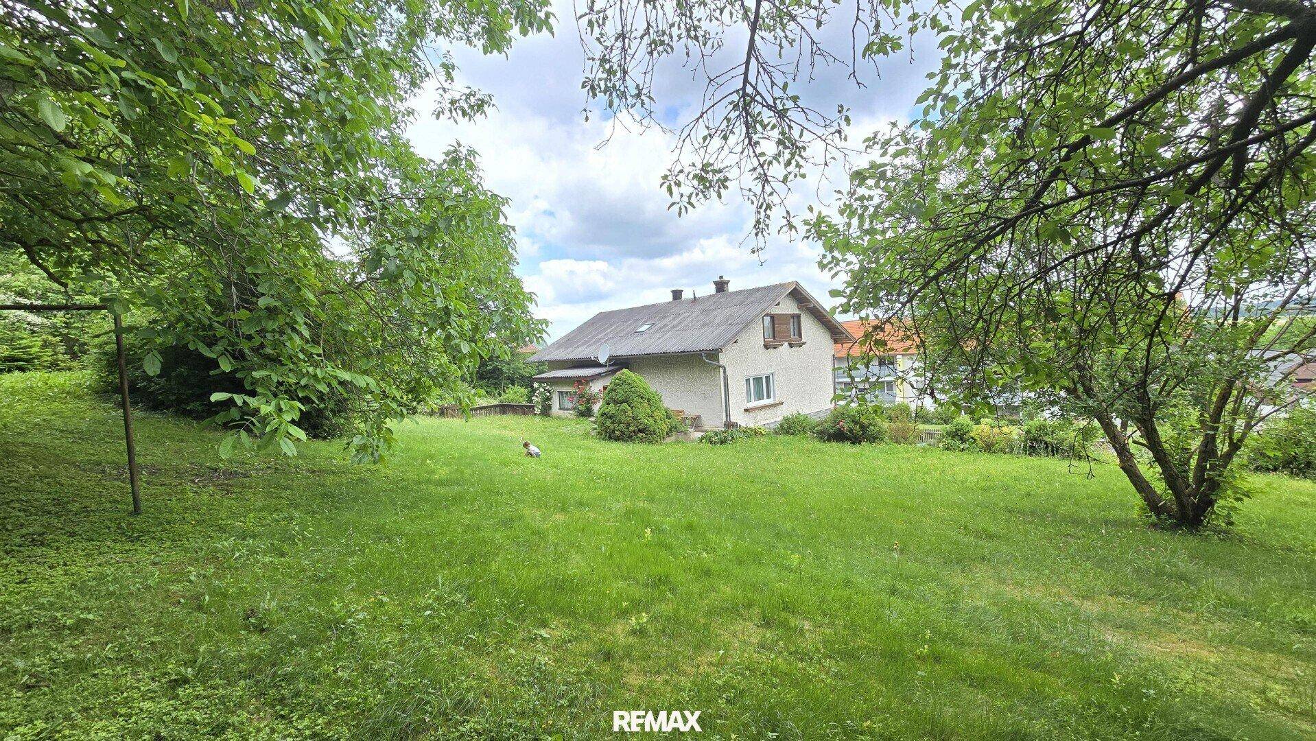 Das Haus von der großen, grünen Gartenfläche aus gesehen, umgeben von Bäumen.