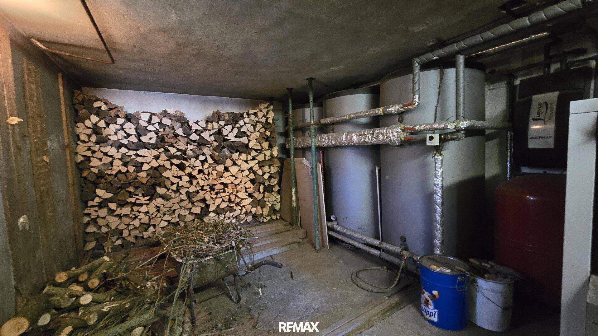 Heizraum mit großen Wassertanks und einem Lagerbereich für Brennholz im Keller.