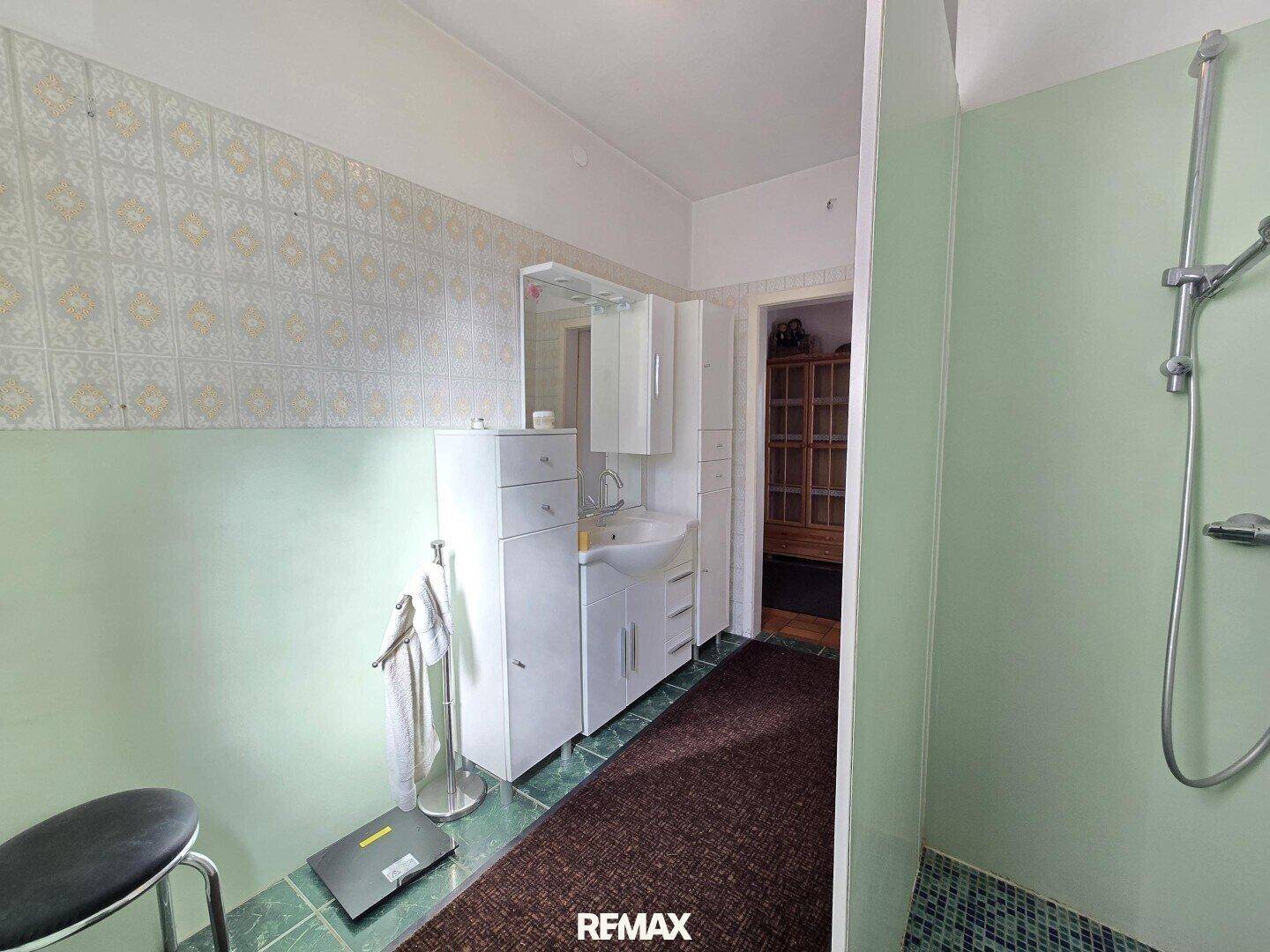 Badezimmer mit Dusche, Waschbecken und hellgrünen Wandfliesen.