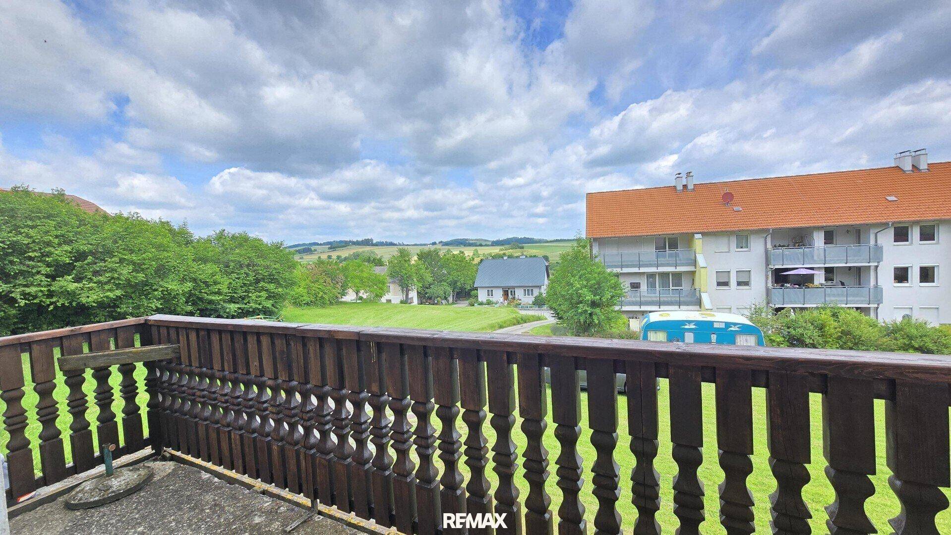 Balkon mit traditionellem Holzgeländer und weitem Blick über die grüne Landschaft und Nachbargebäude.