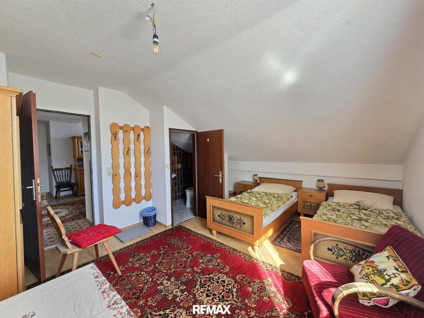 Dachgeschoss-Schlafzimmer mit zwei Betten und Zugang zu einem weiteren Raum.