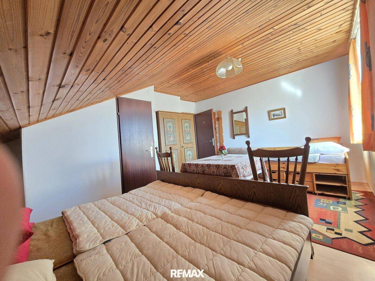 Dachgeschoss-Schlafzimmer mit Holzbalkendecke, Doppelbett und traditioneller Einrichtung.