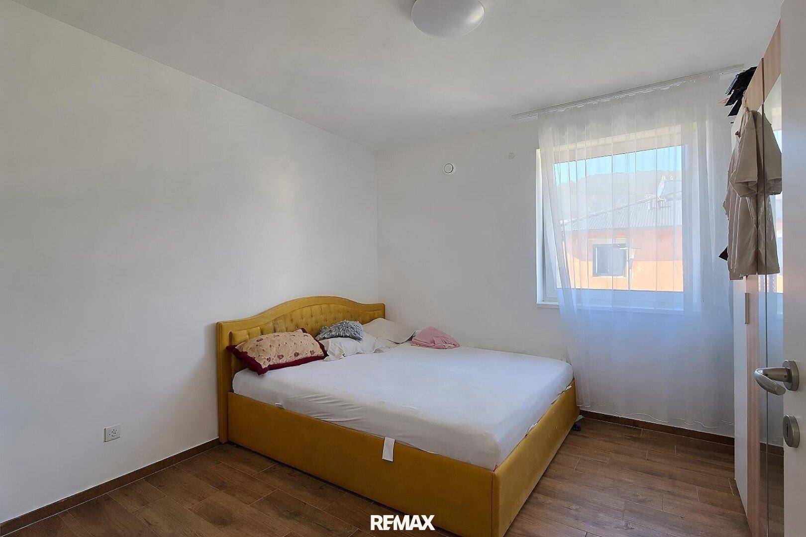 Schlafzimmer mit gelbem Bettrahmen, Holzboden und Fenster mit Blick nach draußen.