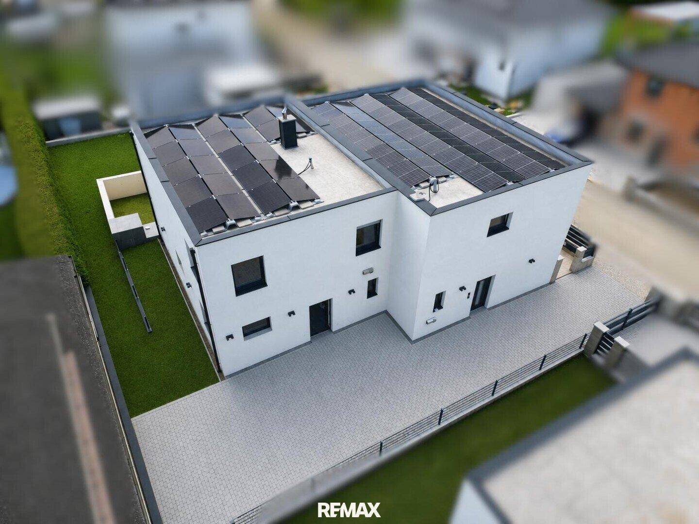 Luftaufnahme eines modernen Hauses mit Photovoltaikanlage und gepflasterter Zufahrt.