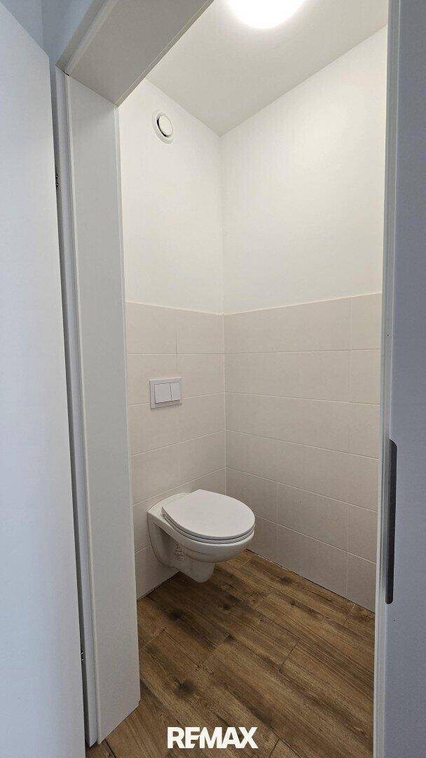 Separate Toilette mit Wand-WC und halbhoch gefliesten Wänden.