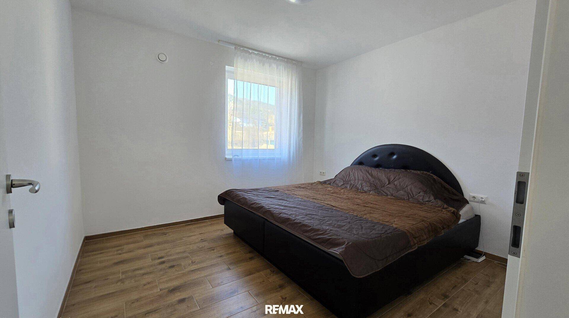 Schlafzimmer mit dunklem Bettrahmen, Holzboden und Fenster.