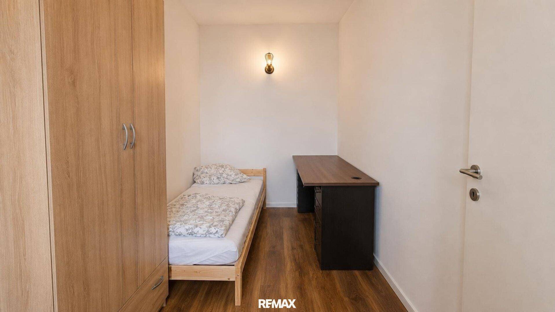 Kleines Schlafzimmer mit Einzelbett, Holzschrank und einem Schreibtisch.