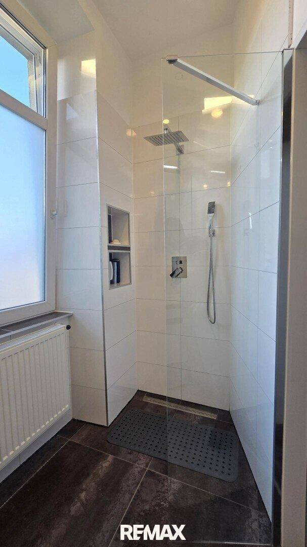 Helles Badezimmer mit ebenerdiger Dusche und Fenster.