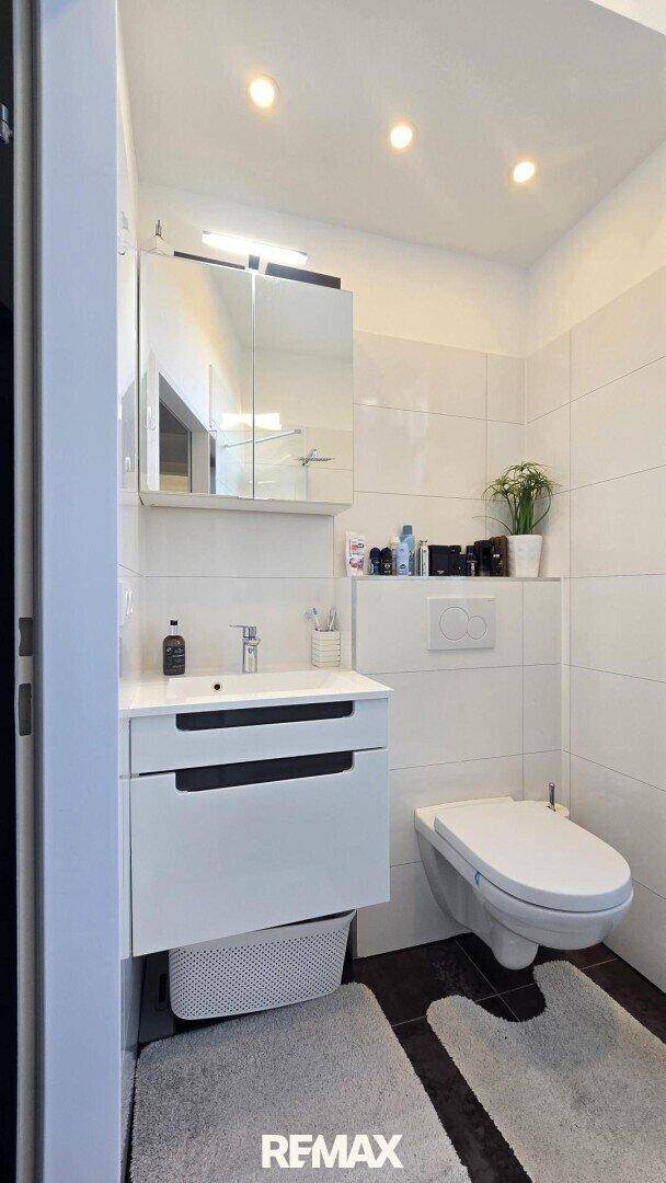 Modernes Badezimmer mit wandhängendem WC, Einzelwaschbecken und Spiegelschrank.