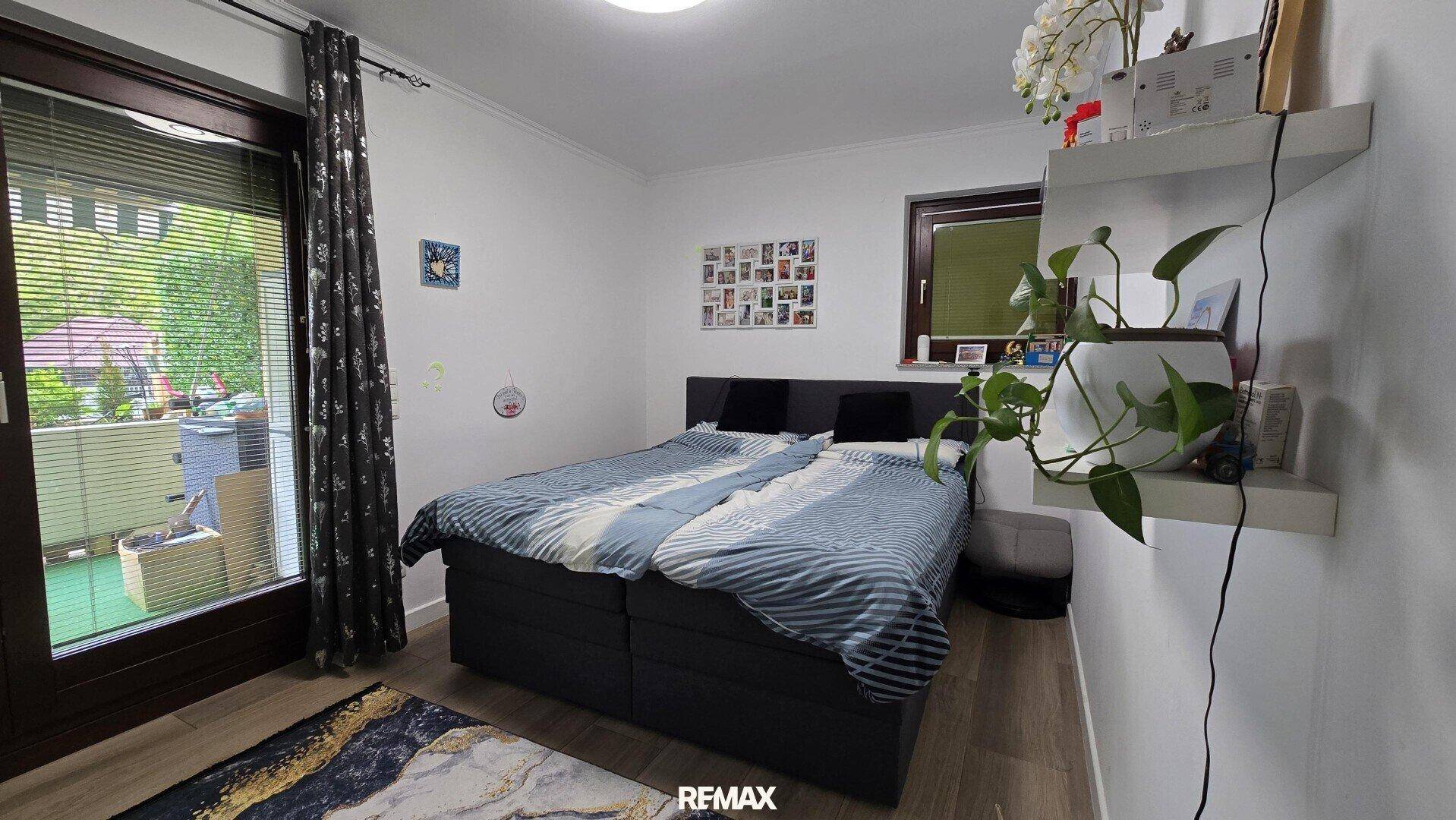 Schlafzimmer mit Doppelbett, Zugang zum Balkon und hellem Holzboden.