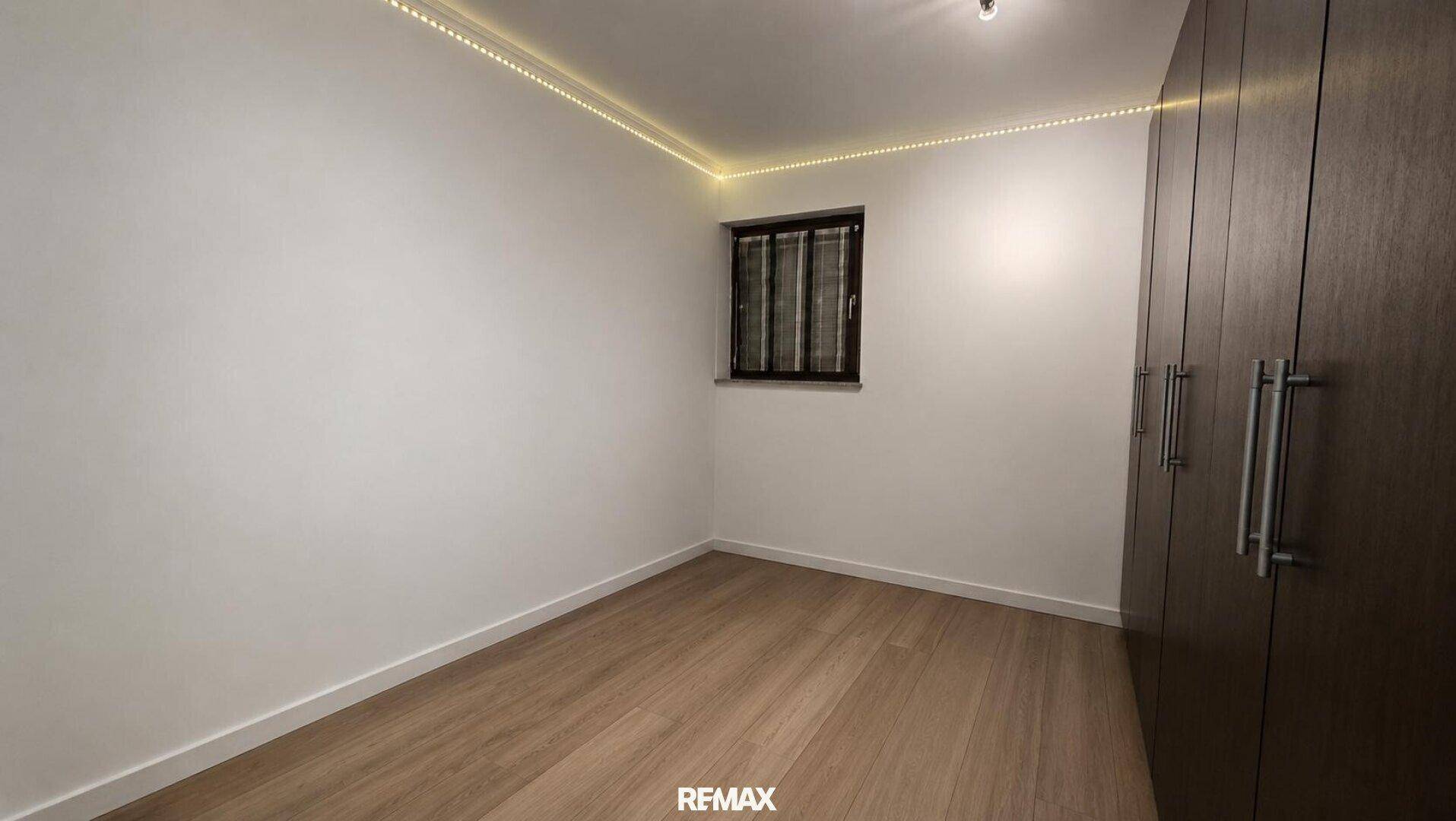 Helles Schlafzimmer mit Einbauschrank, hellem Holzboden und indirekter Deckenbeleuchtung.