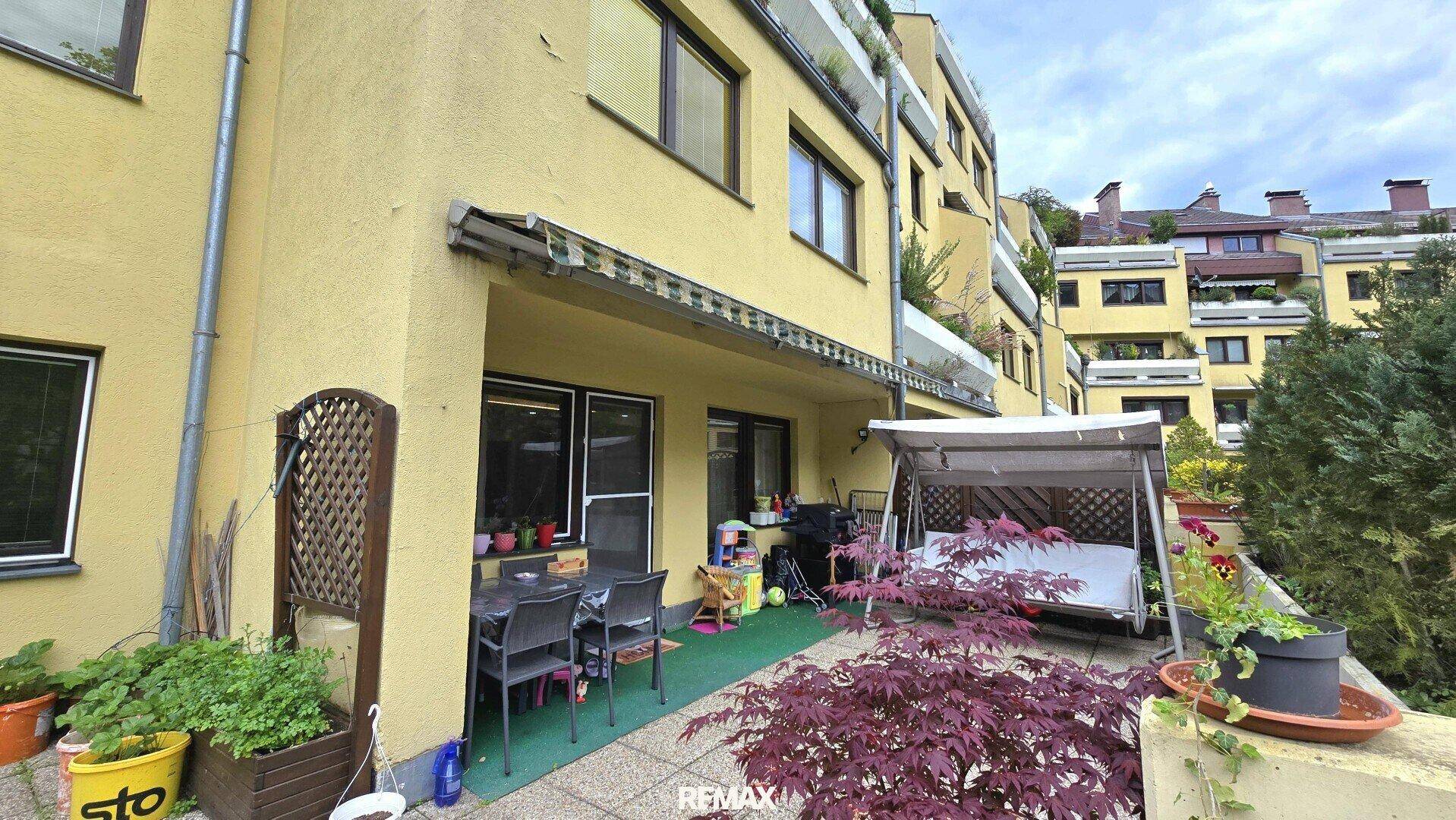 Geräumige Terrasse mit Sitzgelegenheiten, Schaukel und Blick auf die Wohnanlage und viel Grün.