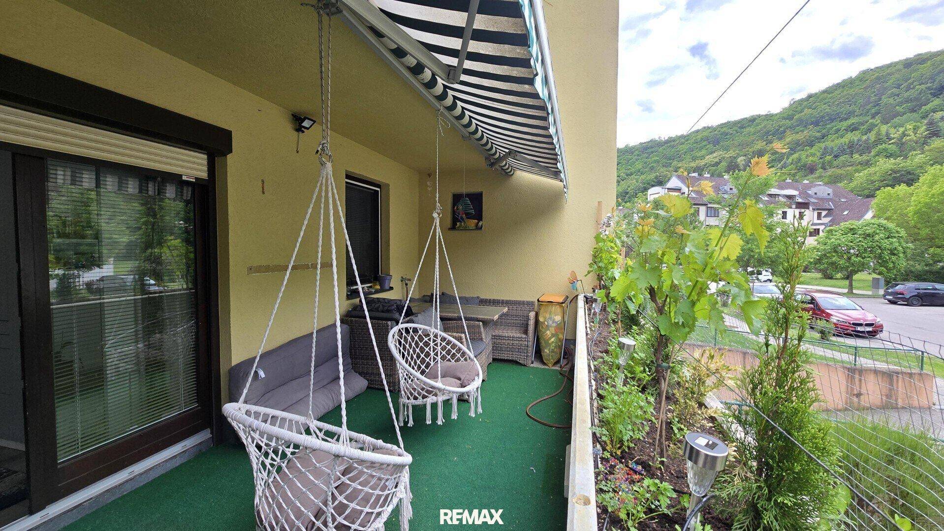 Gemütlicher Balkon mit Hängesesseln, Kunstrasen und Blick auf die grüne Umgebung und Straße.