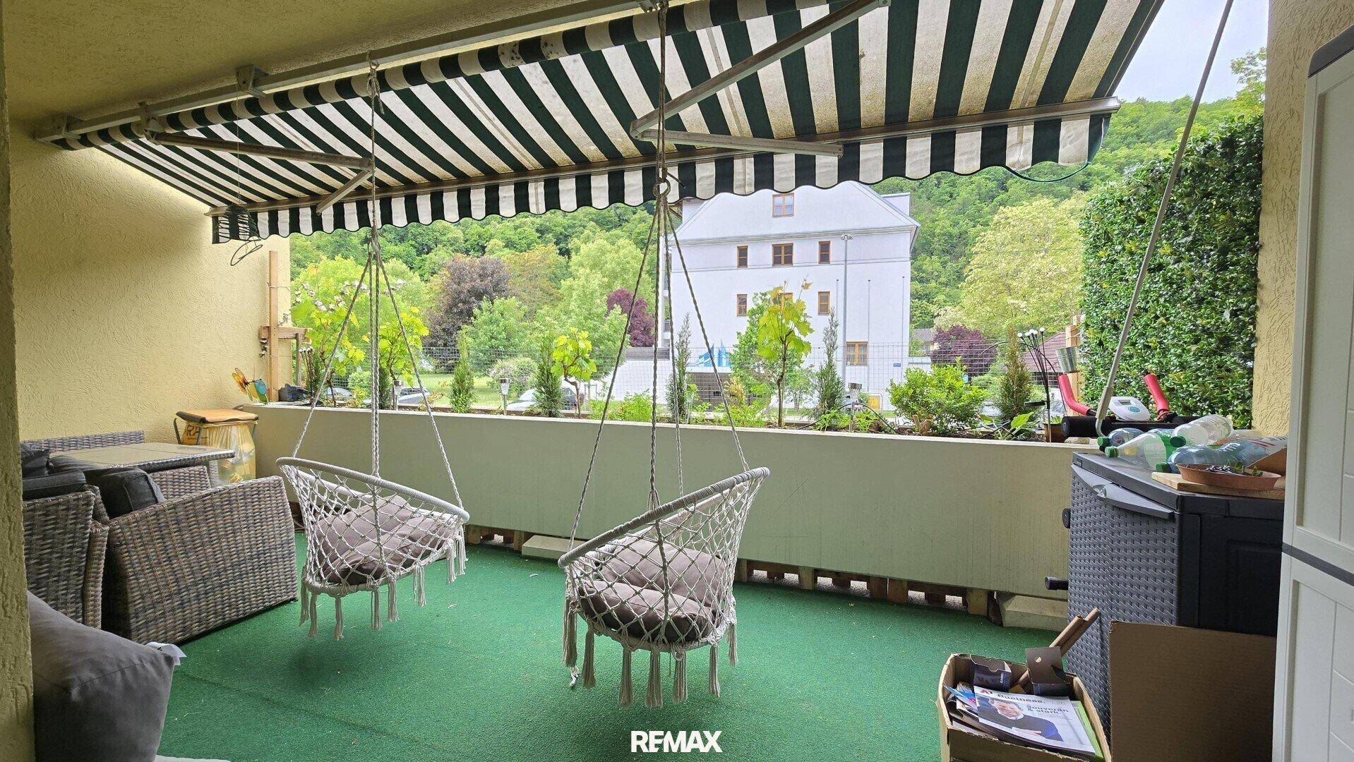 Überdachter Balkon mit Hängesesseln, Kunstrasen und Blick auf die grüne Umgebung.