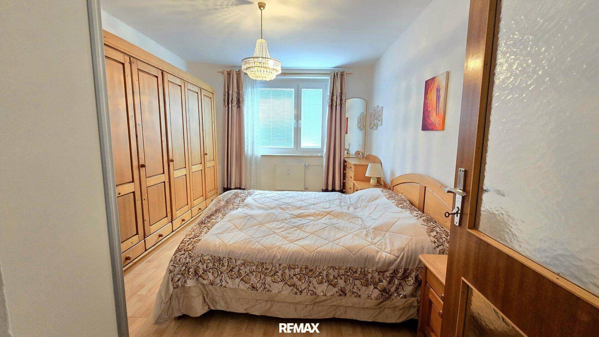 Schlafzimmer mit großem Kleiderschrank, Doppelbett und Fenster mit Vorhängen.