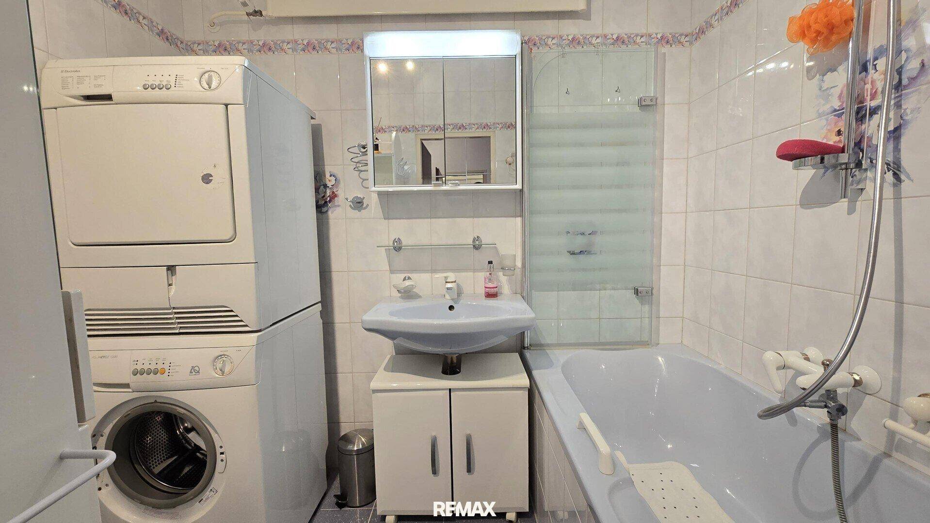 Badezimmer mit Badewanne, Waschbecken, Waschmaschine und Trockner, hell gefliest.