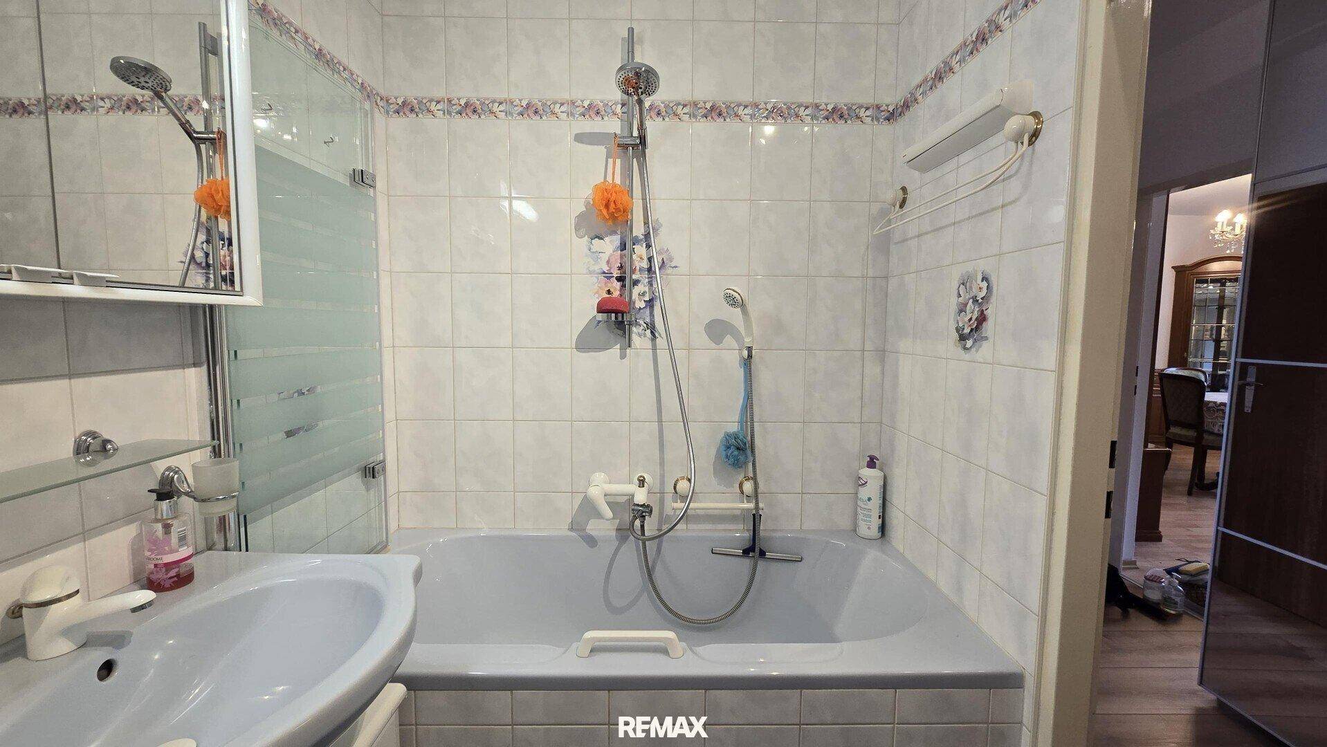 Badezimmer mit Badewanne, Duschvorrichtung und Waschbecken, hell gefliest.