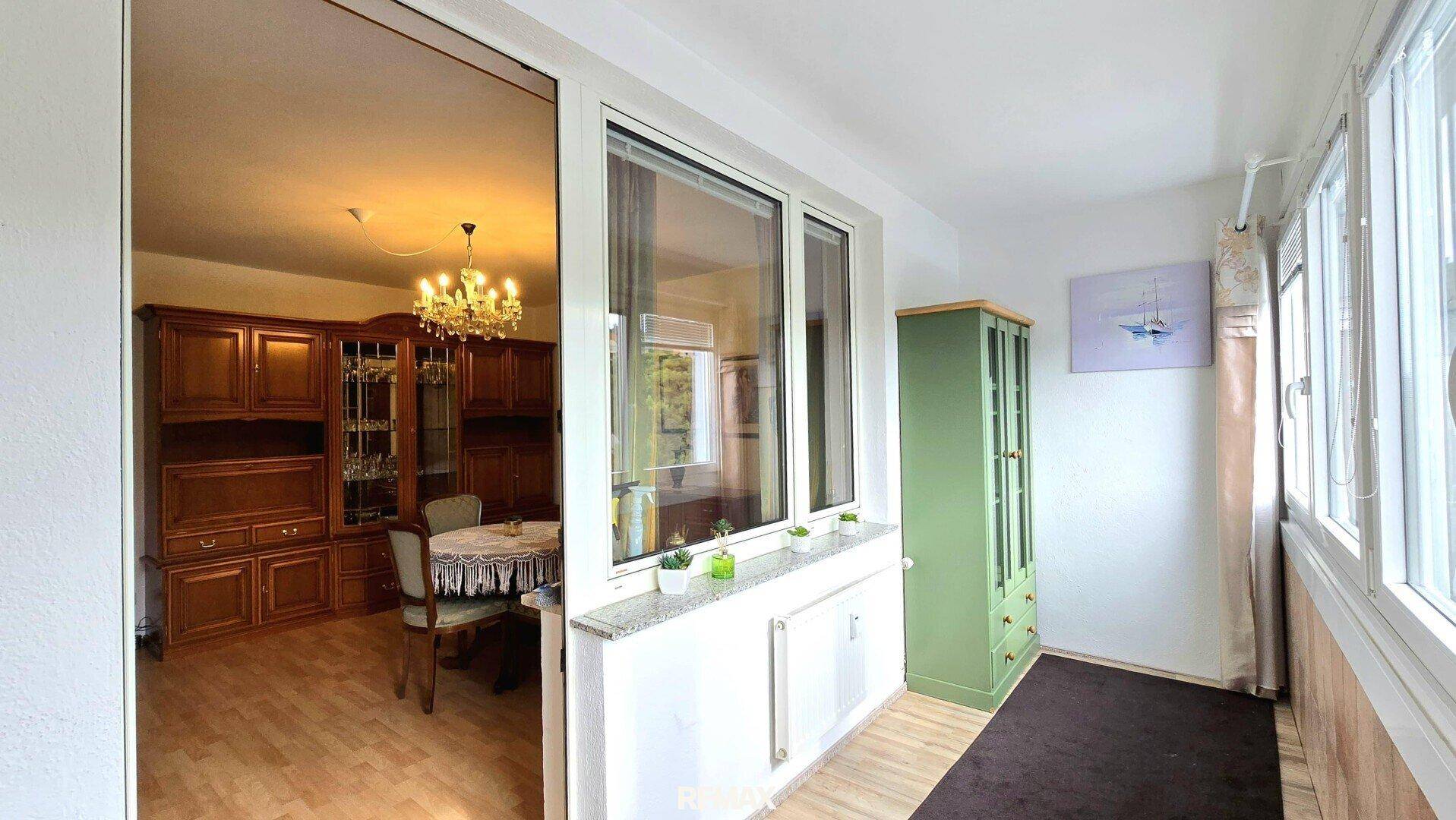 Verglaste Loggia mit Blick zurück in den Wohnbereich, ausgestattet mit Fliesenboden und Fensterfront.