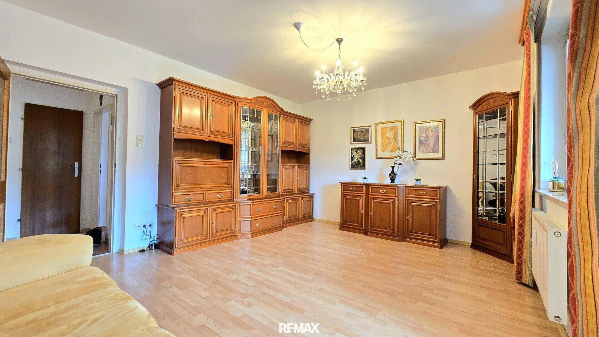 Geräumiges Wohnzimmer mit traditionellen Holzmöbeln, Laminatboden und einem Kronleuchter.