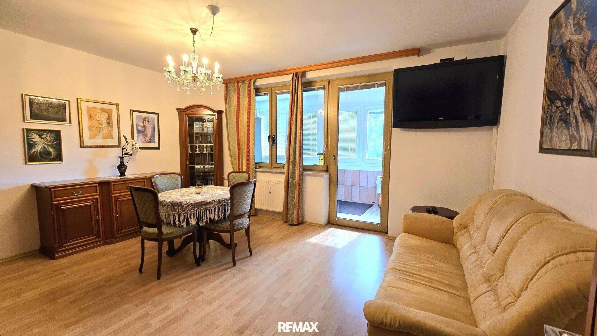 Gemütlicher Wohn-Essbereich mit Sofa, Esstisch und Zugang zu einem verglasten Balkon.