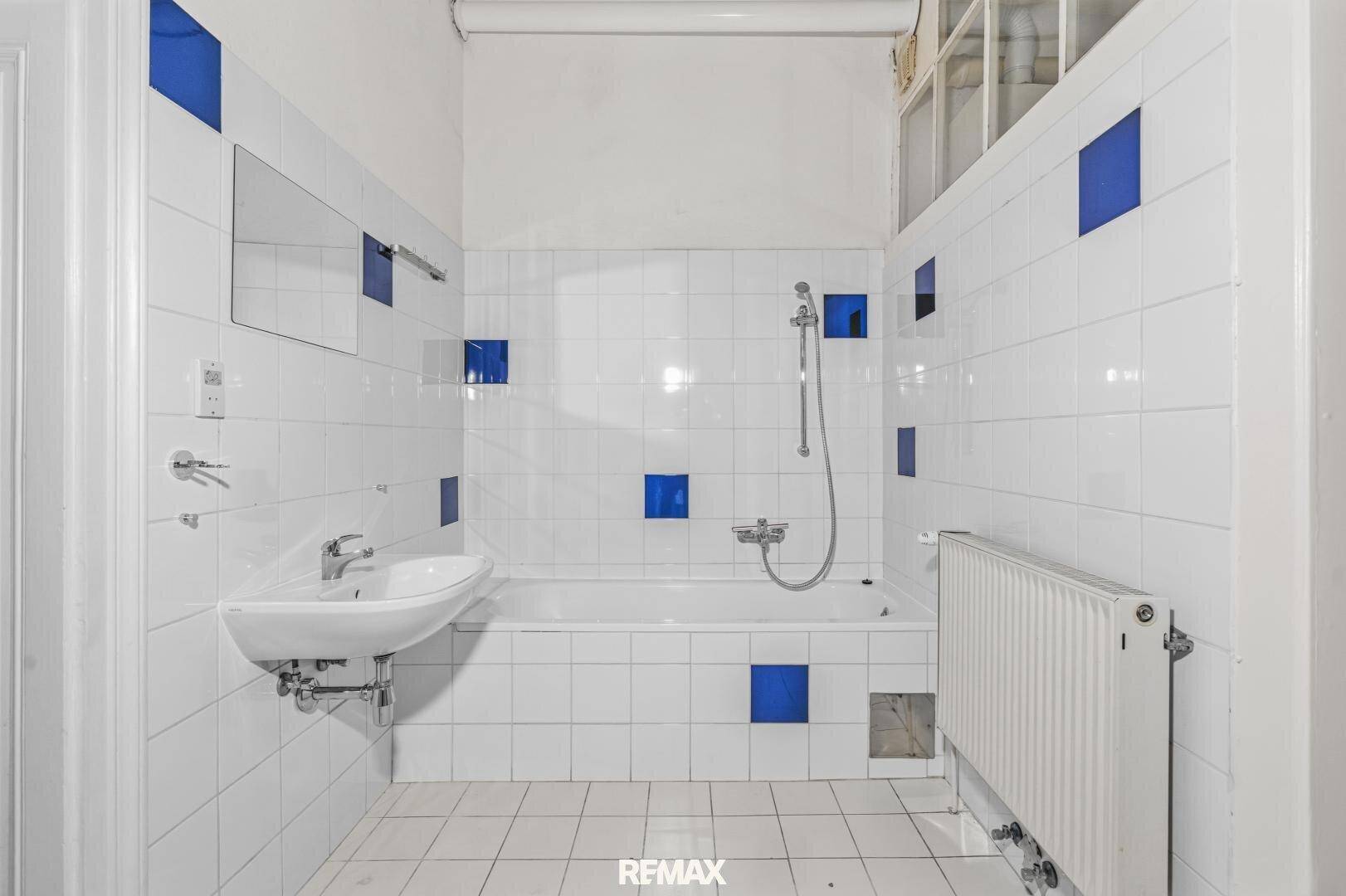 Badezimmer mit weißen Fliesen, blauen Akzenten, Badewanne mit Duschfunktion und Heizkörper.
