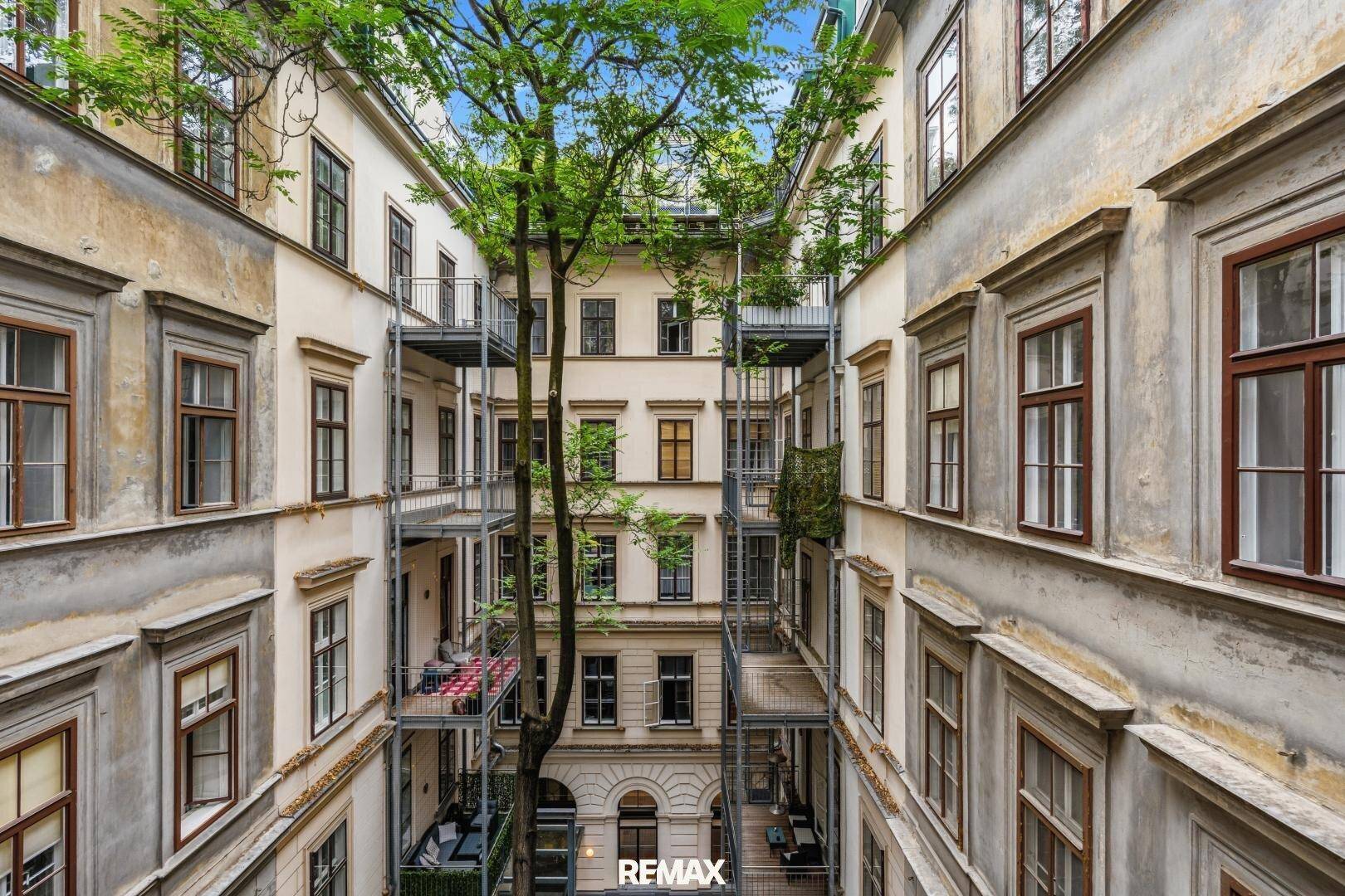 Grüner Innenhof mit mehreren Balkonen und einem großen Baum, der für Schatten sorgt.