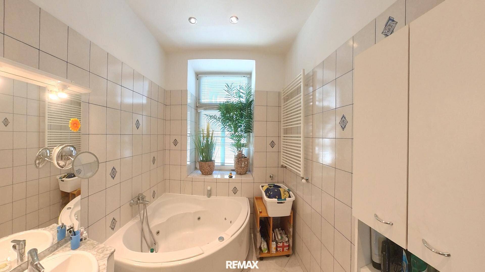 Gefliestes Badezimmer mit Eckbadewanne, Doppelwaschbecken und Fenster für Tageslicht.
