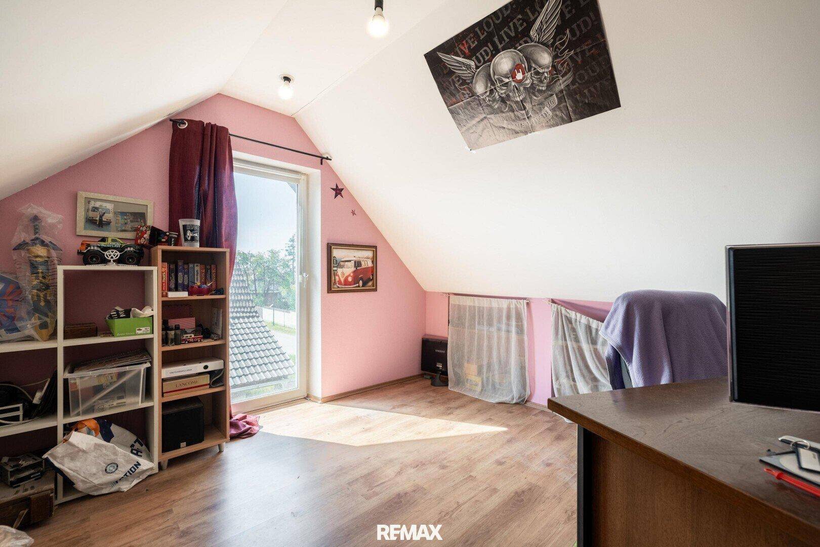 Kinderzimmer im Dachgeschoss mit rosa Wänden, Schräge und Zugang nach draußen.