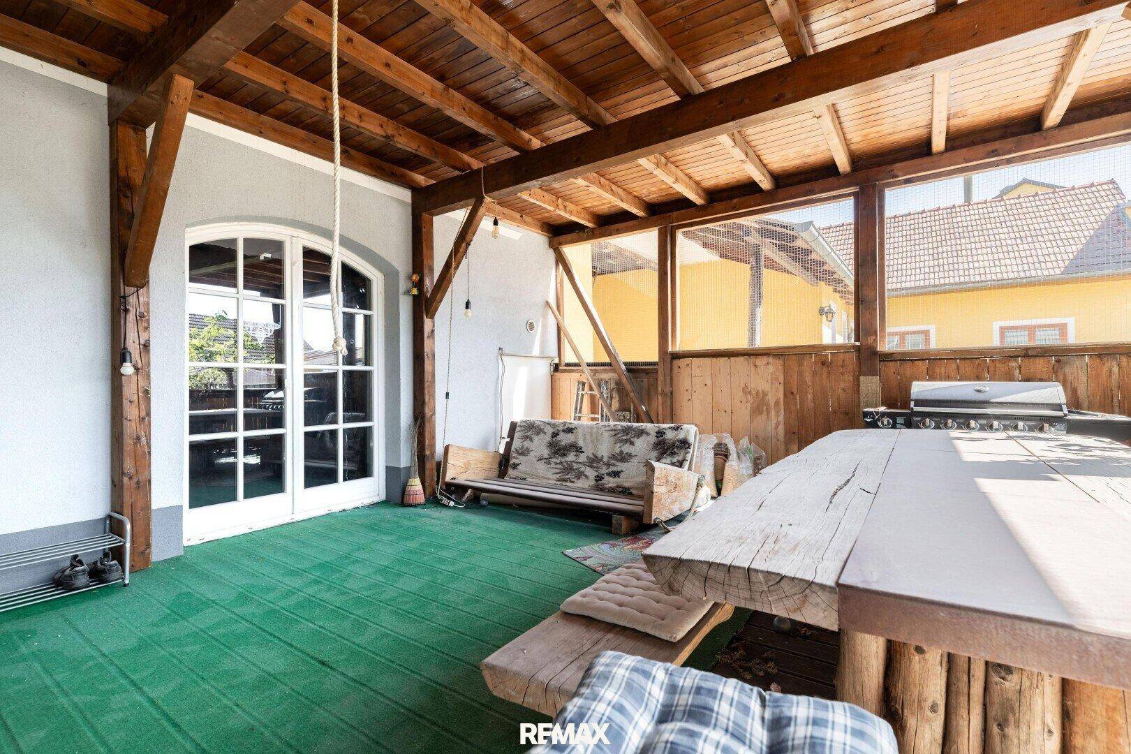 Überdachte Terrasse mit Holzbalken, Sitzgelegenheiten und Grillbereich, ideal für gesellige Abende.
