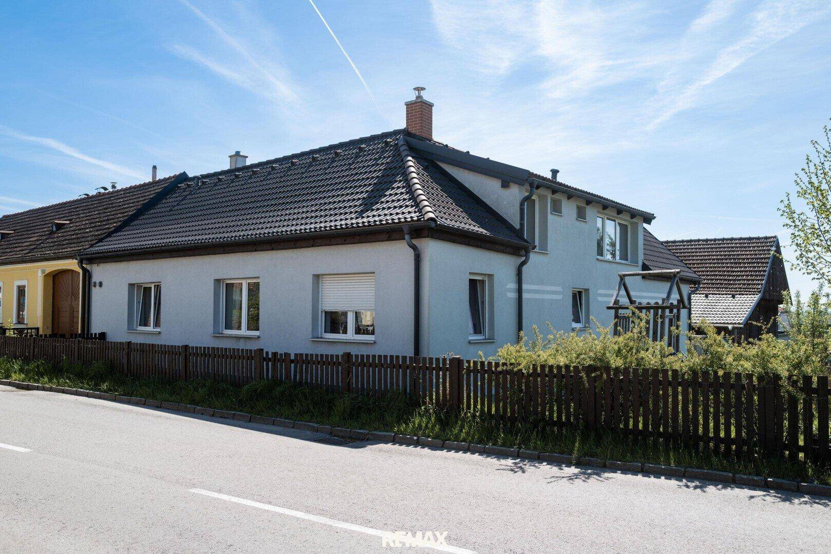 Ansicht des Hauses von der Straße mit Zaun und Rollläden an den Fenstern.