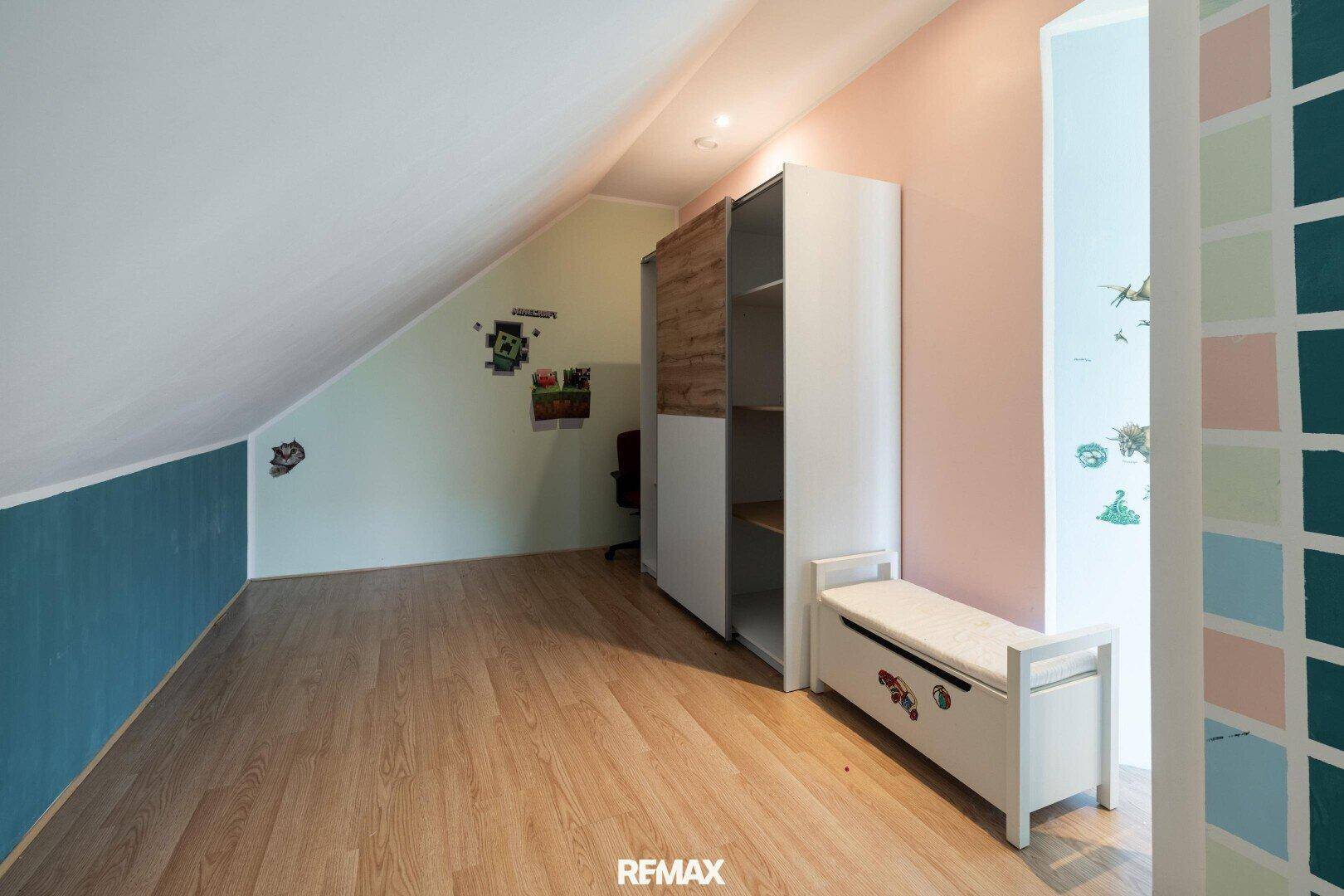 Kinderzimmer im Dachgeschoss mit Schrank, Sitzbank und farbigen Wänden.
