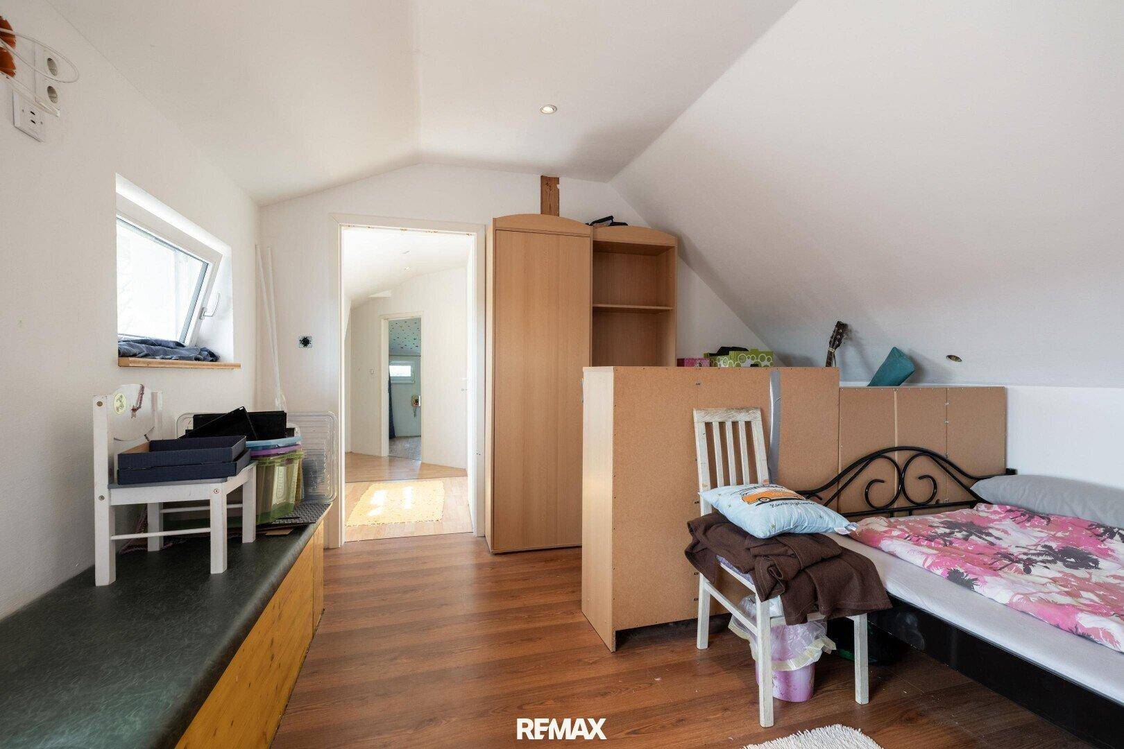 Schlafzimmer im Dachgeschoss mit Bett, Schrank und Zugang zum Flur.