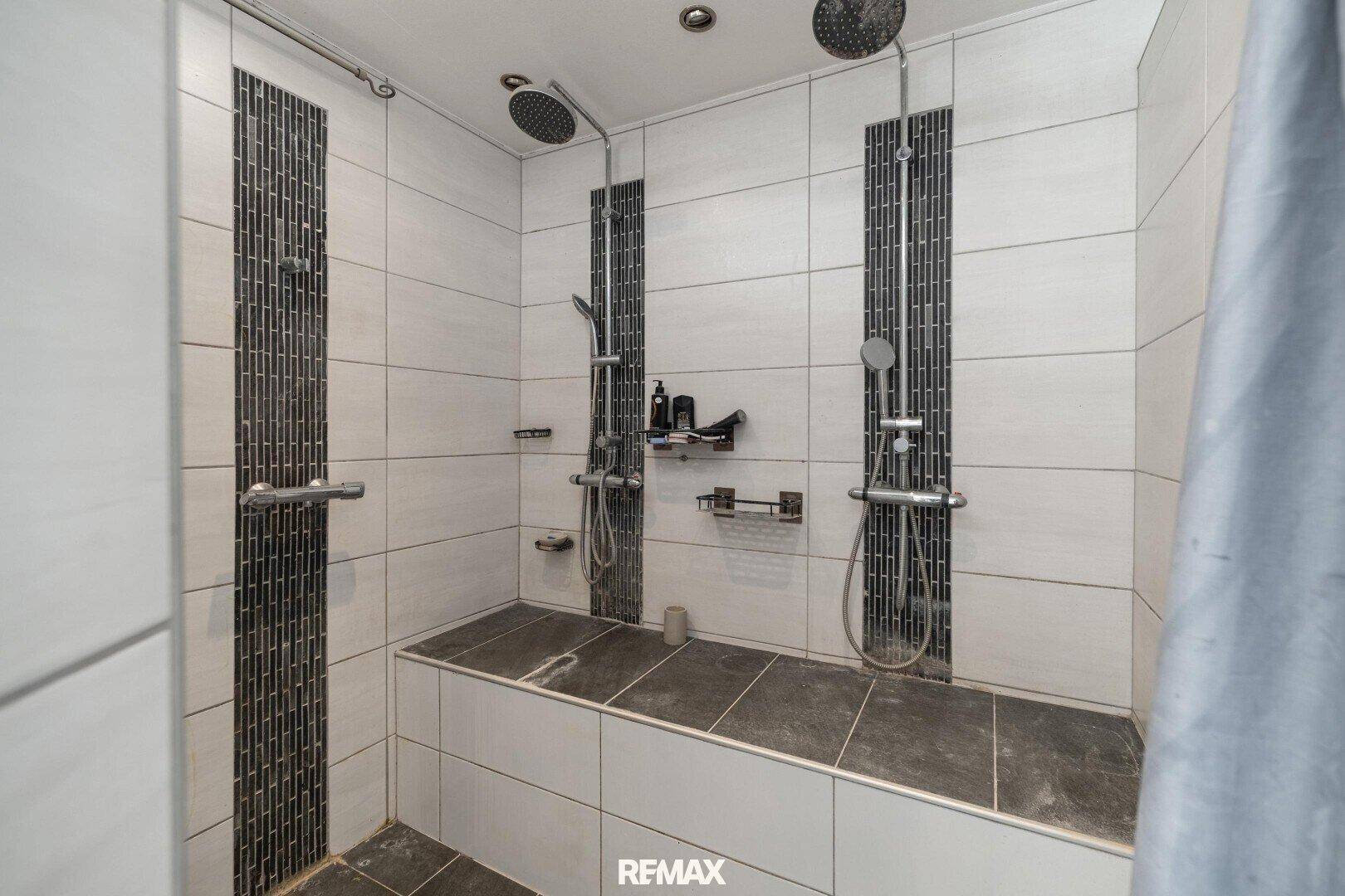Modernes Badezimmer mit zwei Regenduschen und dunklen Akzentfliesen.