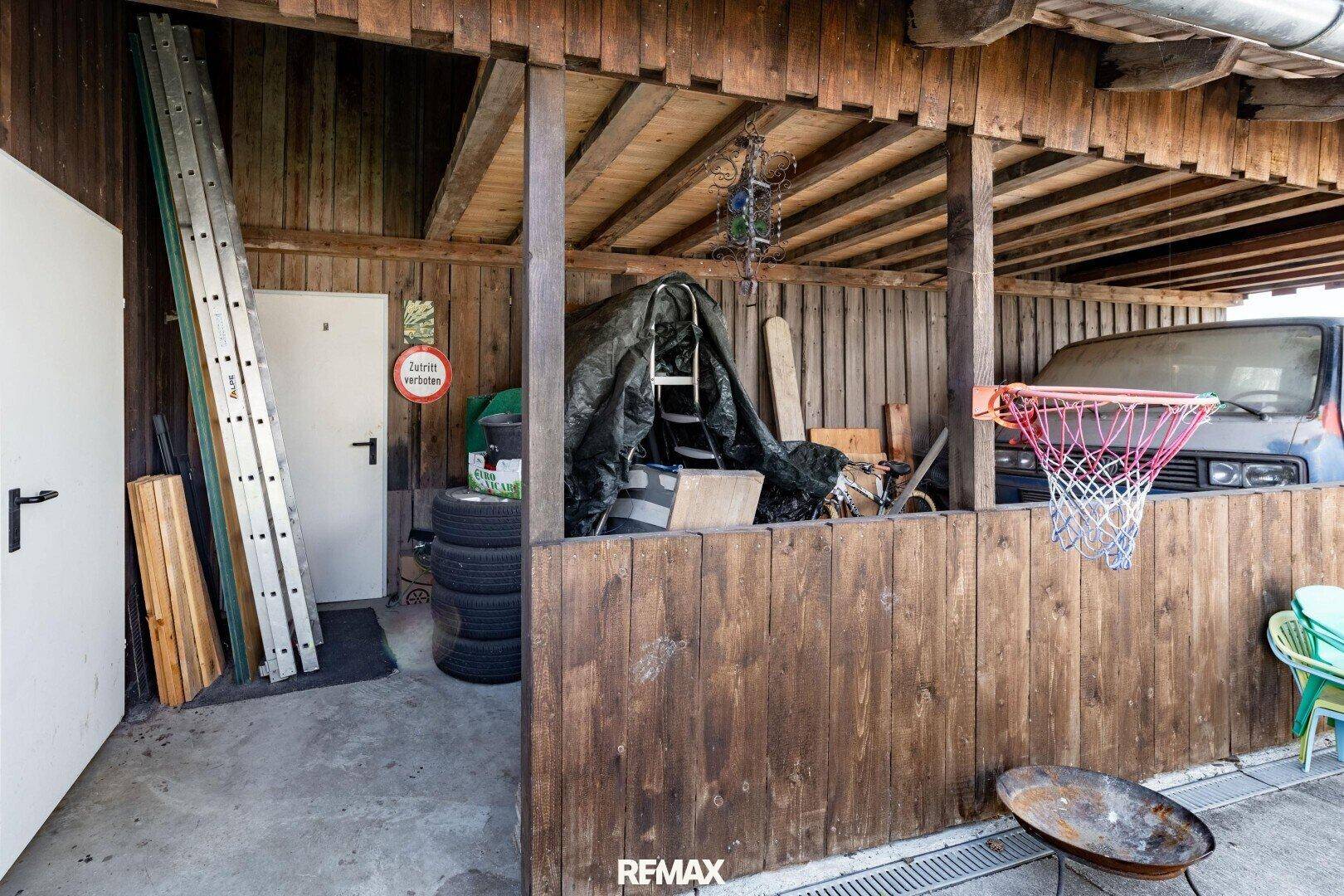 Überdachter Abstellbereich mit Holzverkleidung, Leiter und Reifen, dient als praktischer Stauraum.