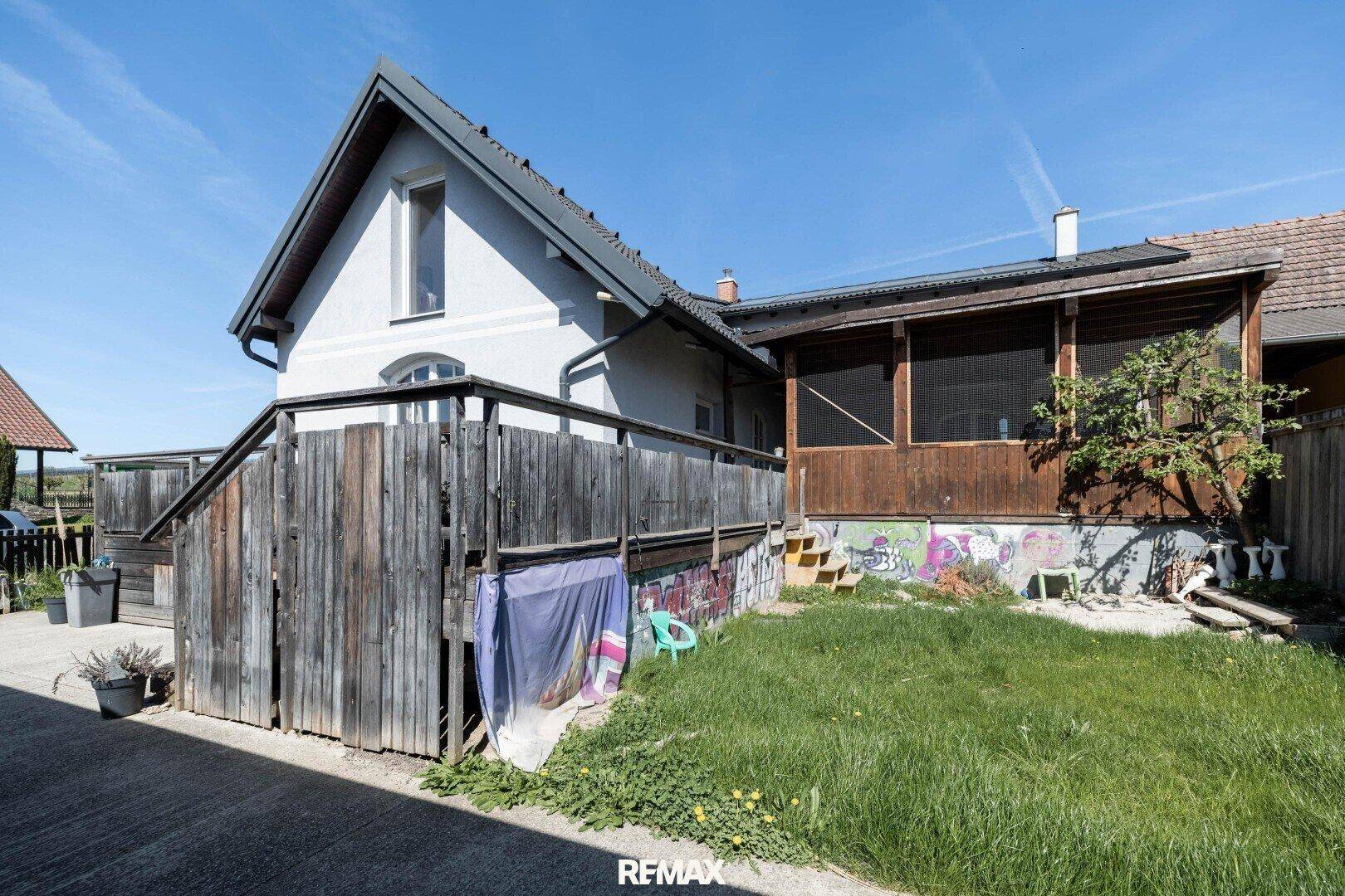 Hinterhof mit Holzterrasse, Treppe und grünem Rasen unter blauem Himmel.