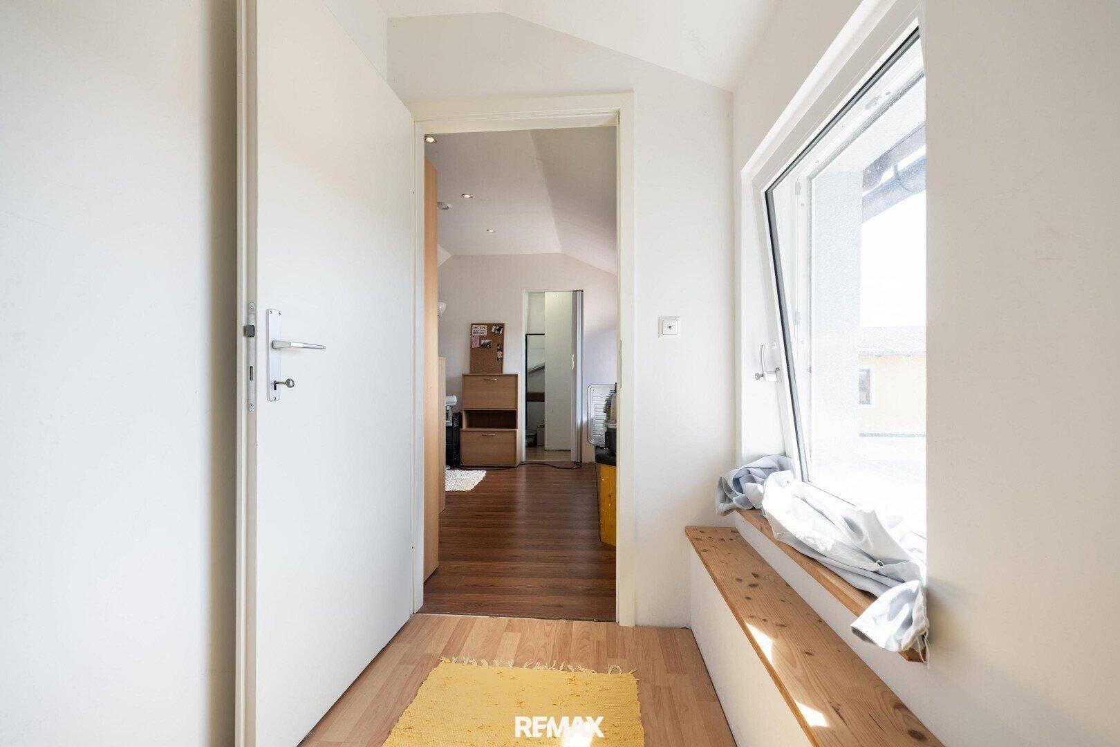 Heller Flur im Dachgeschoss mit Fensterbank und Zugang zu weiteren Zimmern.
