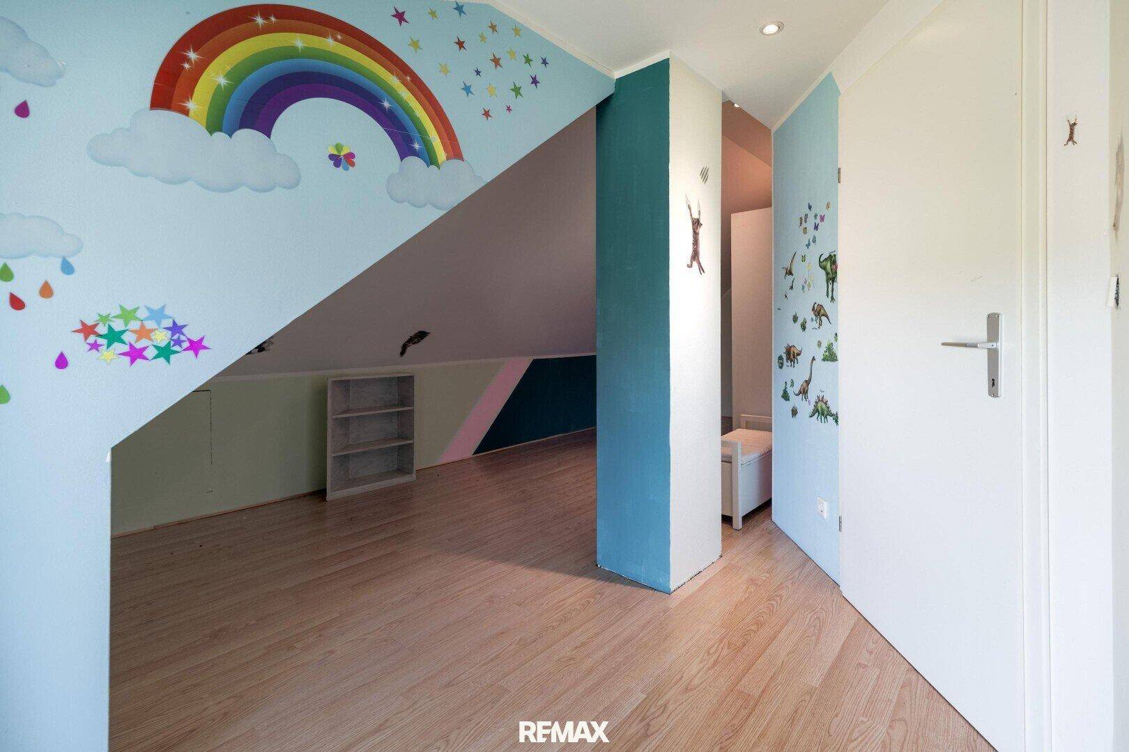 Buntes Kinderzimmer im Dachgeschoss mit Regenbogen-Wandmalerei und Holzboden.