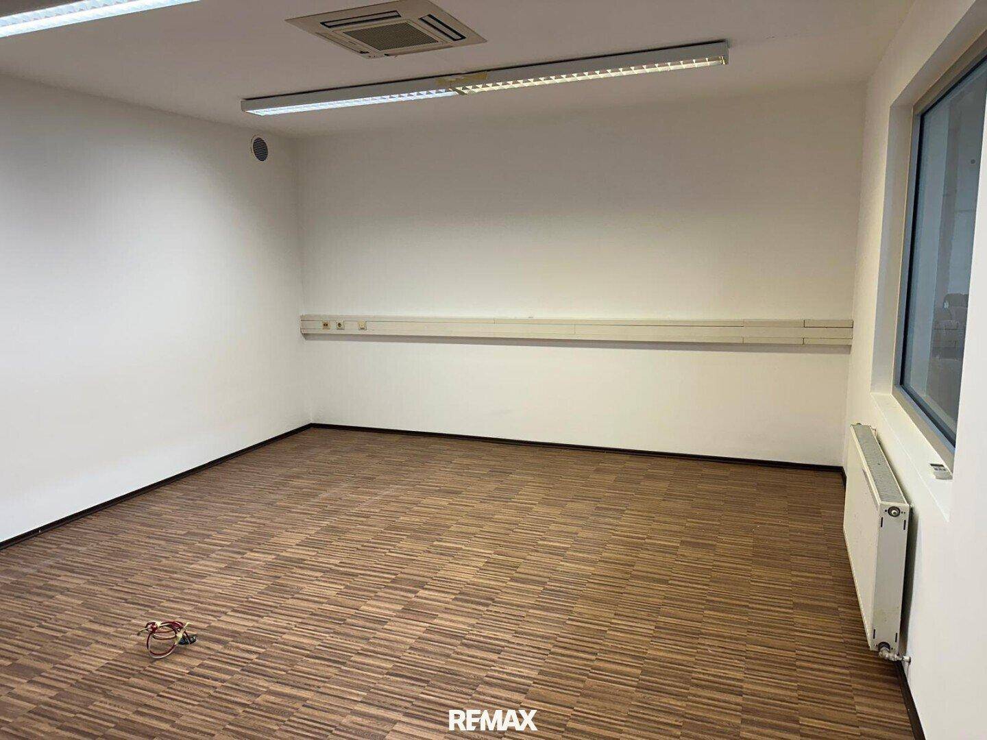 Modernes Büro mit Laminatboden in Holzoptik, Klimaanlage und einem Fenster für Tageslicht.