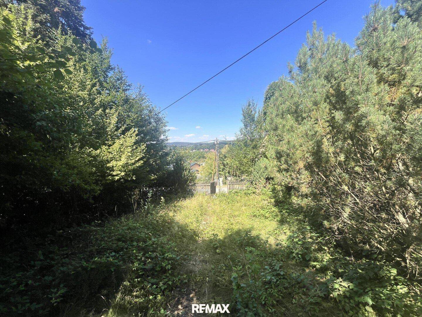 Grundstück mit Blick über eine bewaldete Landschaft und eine Siedlung in der Ferne unter blauem Himmel.