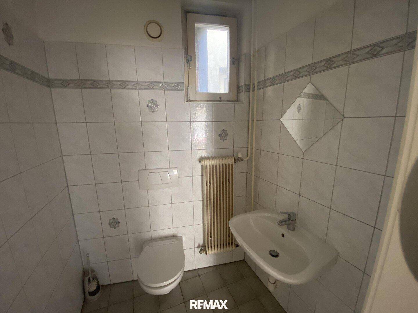 Separates WC mit Toilette, Waschbecken, Heizkörper und einem Fenster.