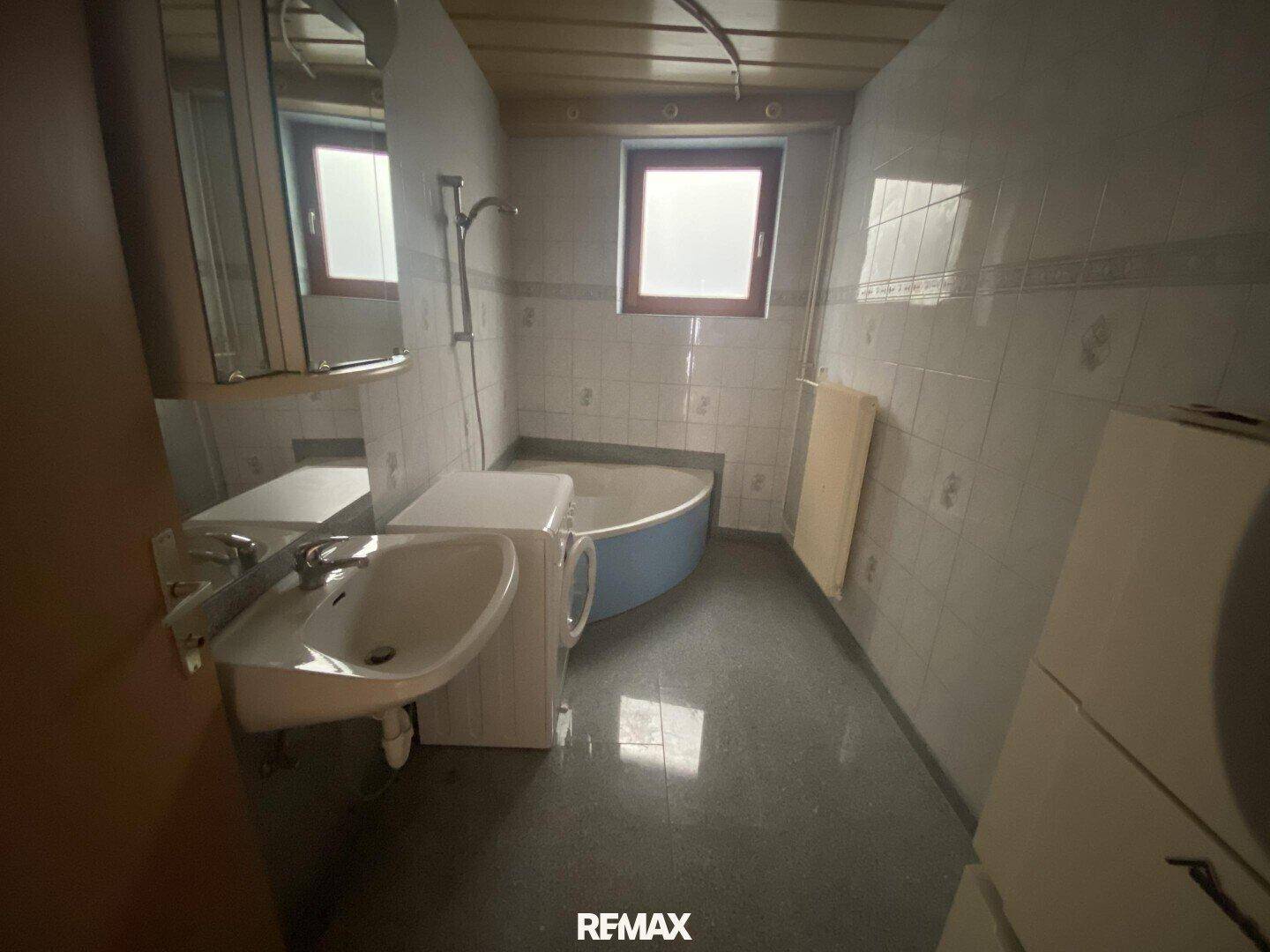 Badezimmer mit Eckbadewanne, Waschbecken, Waschmaschine und einem Fenster.