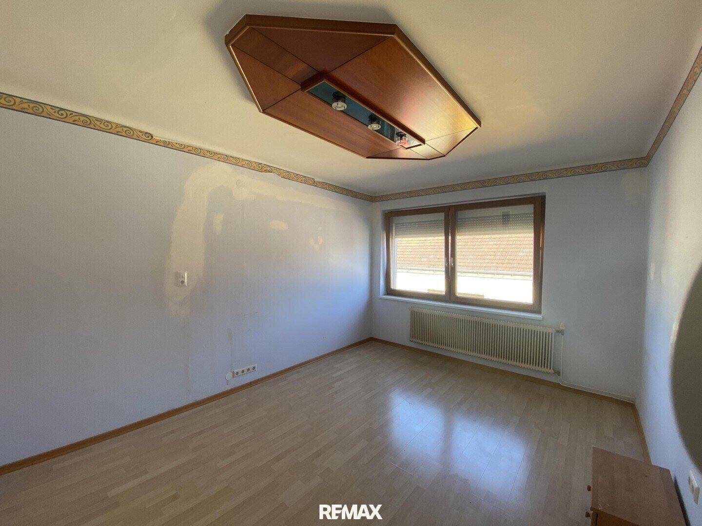Heller Raum mit Laminatboden, Fenster mit Jalousien und einem Heizkörper unter dem Fenster.